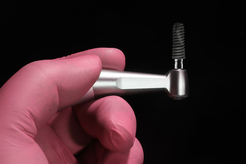 a single dental implant being held up with a tool to place it